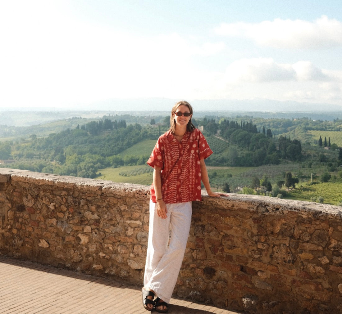Person standing on a stone wall overlooking a scenic landscape with green hills and a clear blue sky.